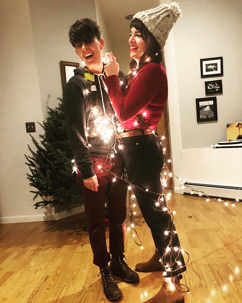 A series of photos of Andrea and Meg on Christmases throughout the years, usually featuring trees, lights, Santa outfits, and dogs in festive sweaters. There are also two red holiday mugs, one that says "Hers", and its pair, that says, "Theirs"