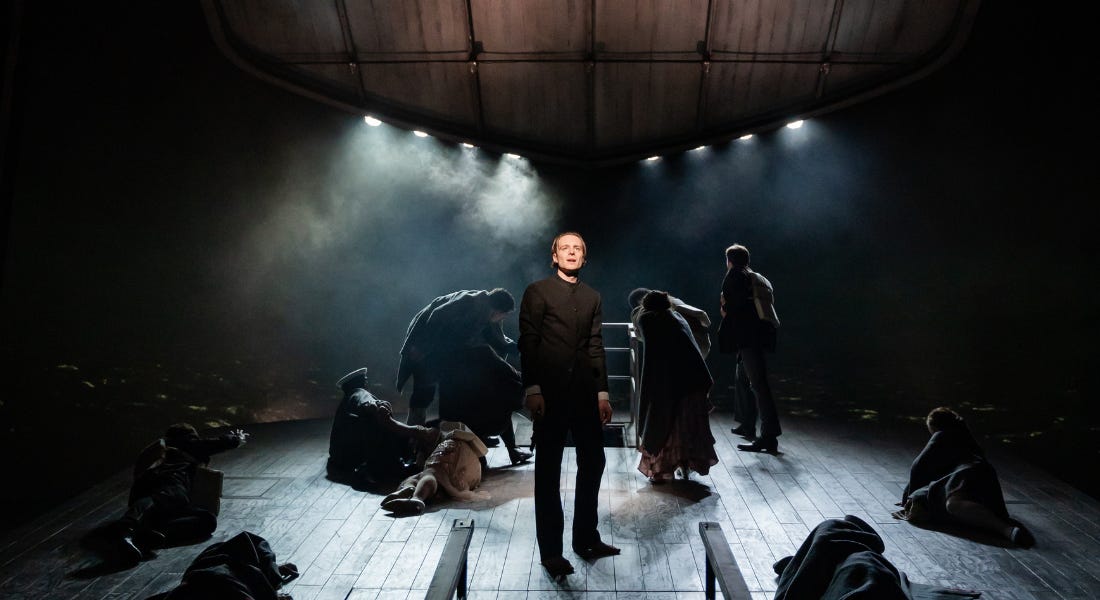 A stage with groups of people on the floor, a man stood in the middle, and wooden decking