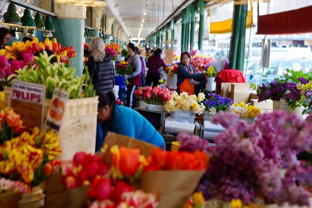A photo of the flowers at Pike Place market. You can see customers and merchants milling about among the colorful blooms.