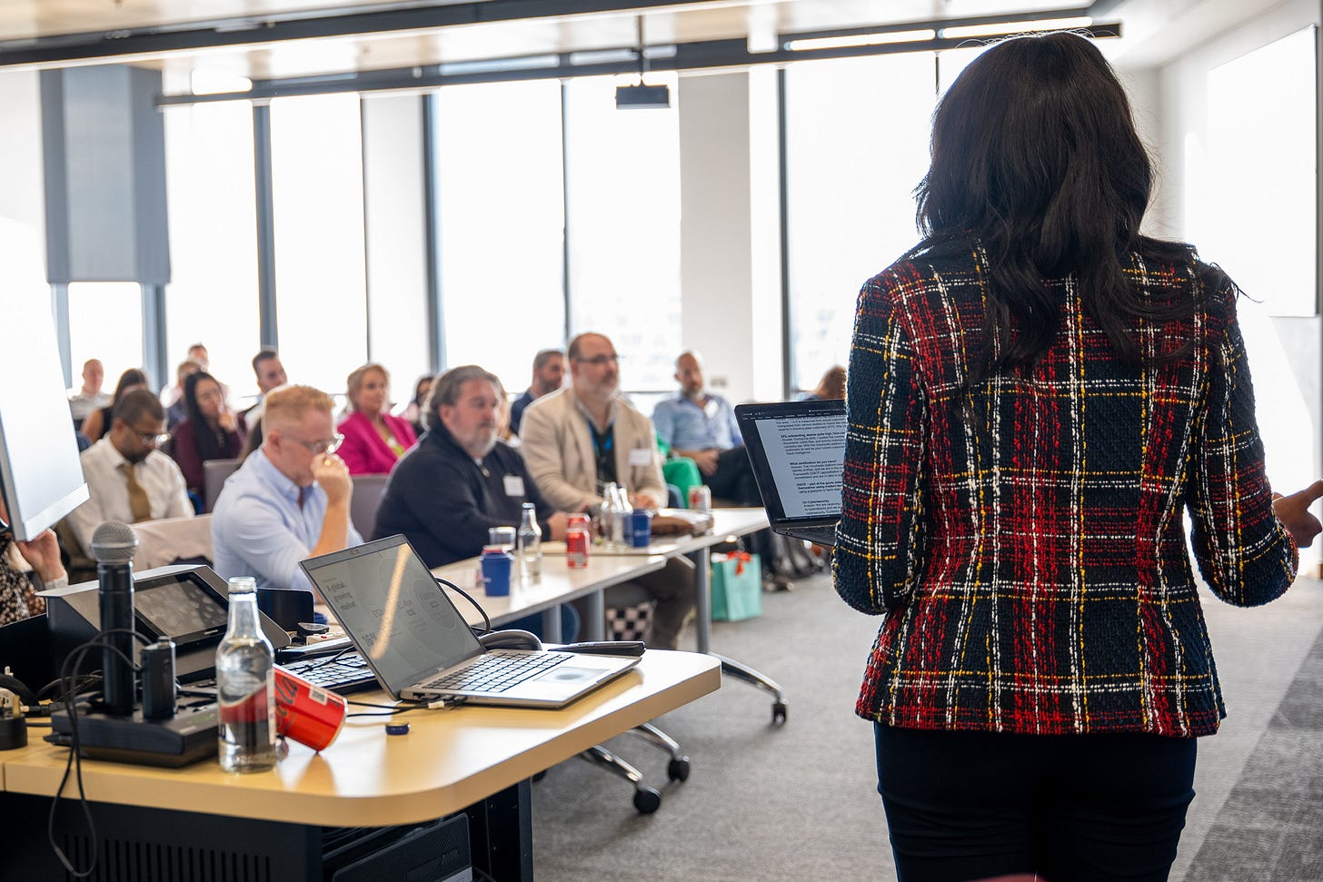 Vouchsafe’s Nkechi with her back to the camera presenting to rows of smartly-dressed people seated in a modern conference room flooded with daylight.
