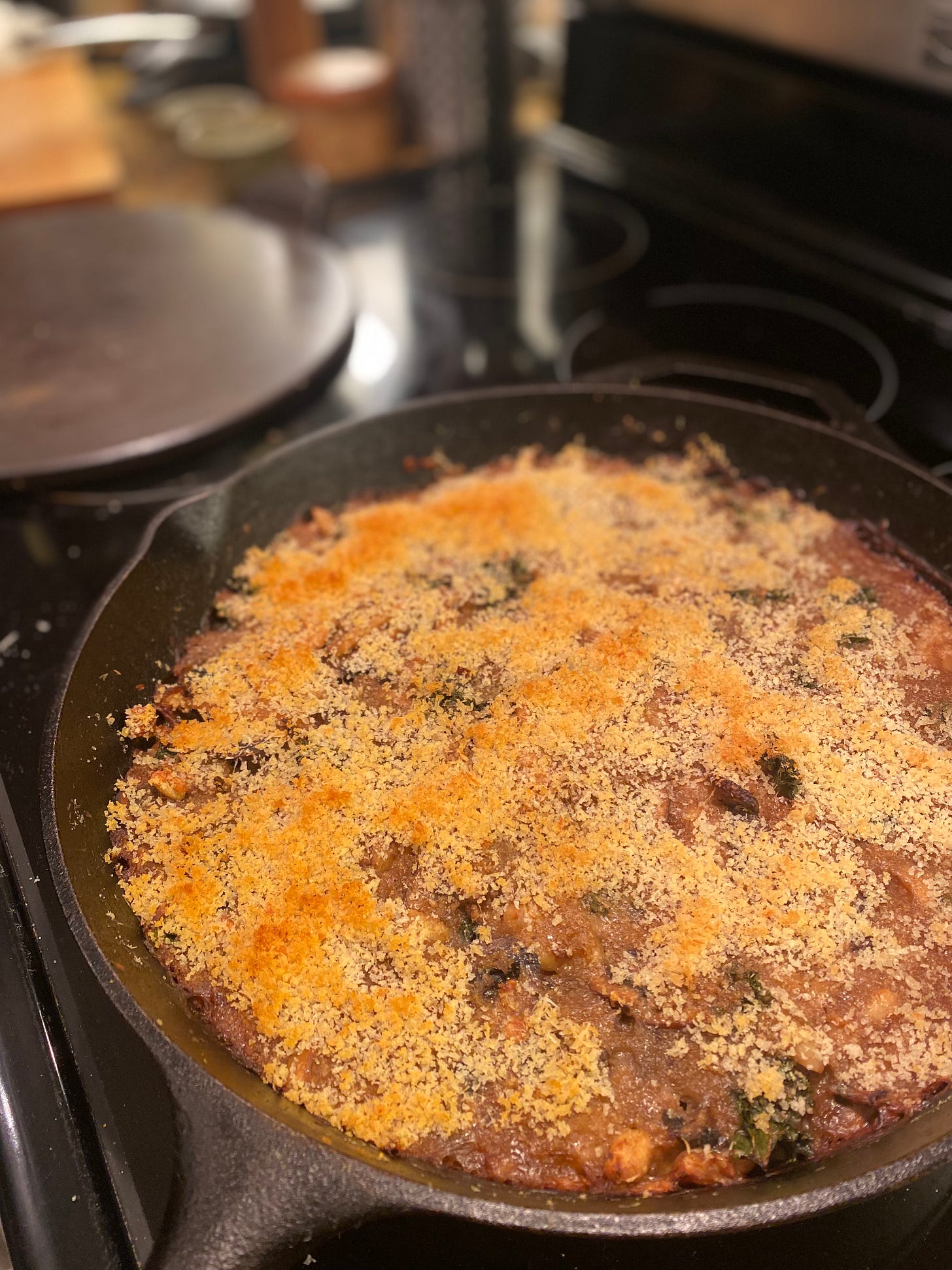A large cast iron pan on the stove with baked beans covered in crispy browned breadcrumbs.