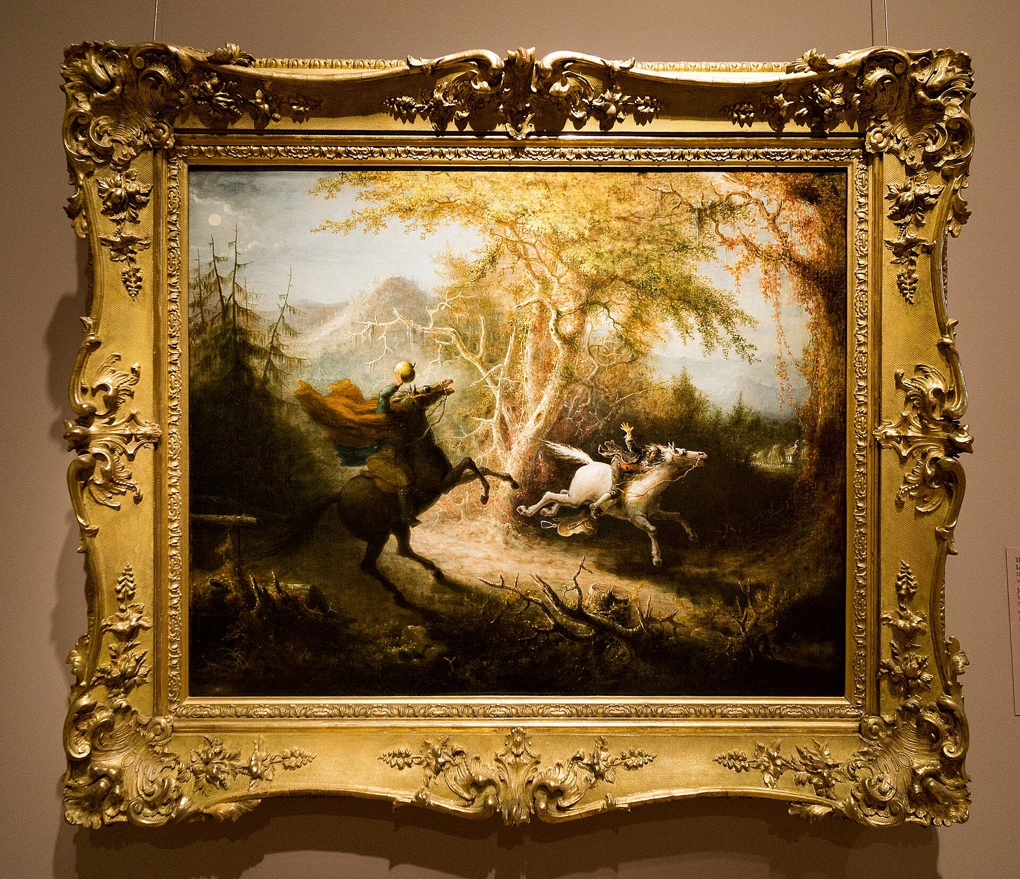 In a dark forest of twisted trees, a thin man on a galloping horse turns in terror toward a black headless rider raising a pumpkin, under a stormy sky. In a dark forest of twisted trees, a thin man on a galloping horse turns in terror toward a black headless rider raising a pumpkin, under a stormy sky.