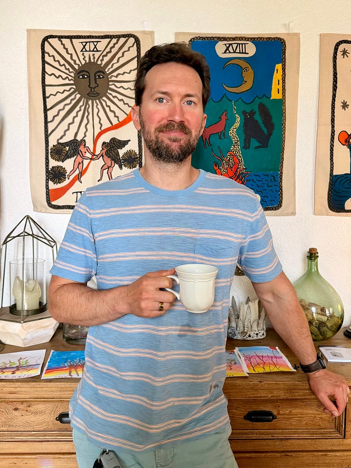 A black rooster in a grassy chicken run, and a man in a blue striped t-shirt holding a coffee mug in front of tapestries.