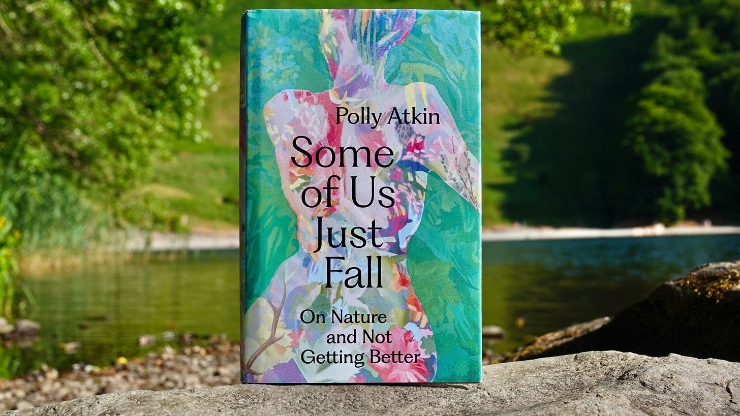 Hardback of Some Of Us Just Fall by Polly Atkin, with a colourful pink, orange, blue and yellow botanical body on a leafy green and blue background, balanced on a rock in a lake, with sunny summery trees and lake seen behind it