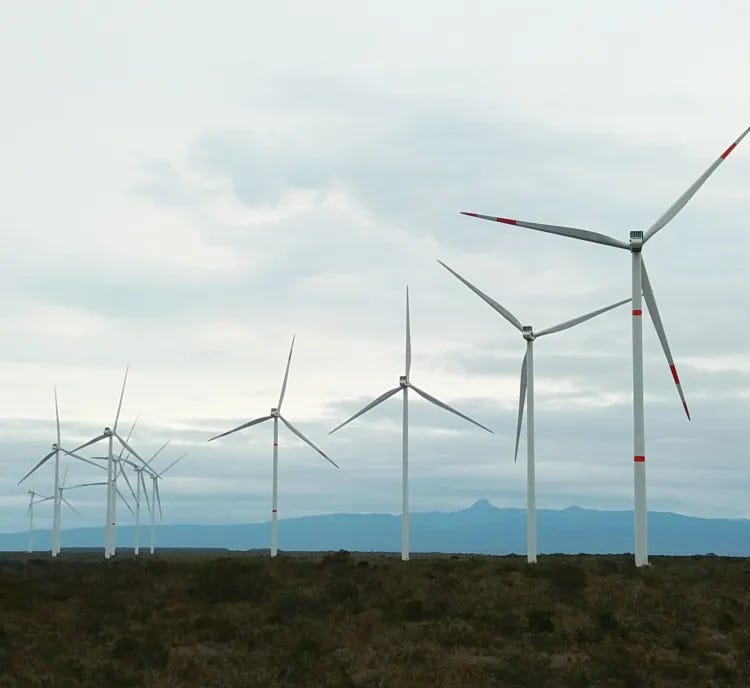 A row of wind turbines on a grassy landscape under a cloudy sky, with mountains visible in the background. A row of wind turbines on a grassy landscape under a cloudy sky, with mountains visible in the background.