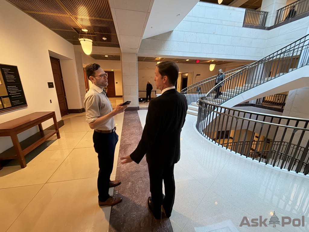 A tieless man in a collared shirt records the answers he's getting from a man in a suit with his arms animated. Photo: Matt Laslo for © www.askapol.com
