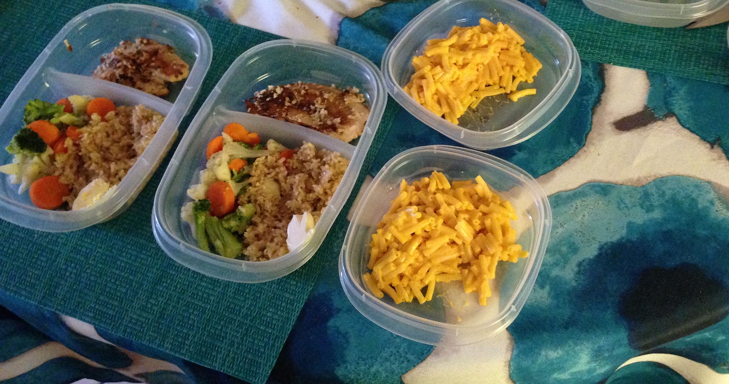 Several divided plastic containers show vegetables, rice, chicken, and macaroni and cheese.
