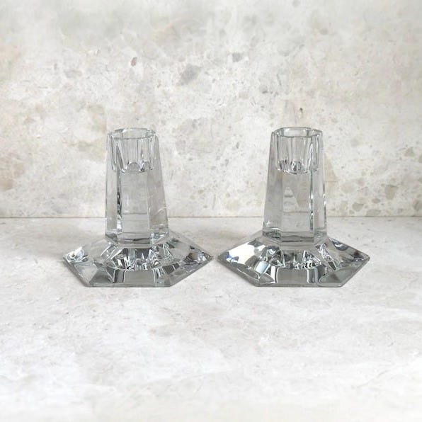 May include: Two clear glass candle holders with octagonal bases. The candle holders are made of faceted glass and have a simple design.