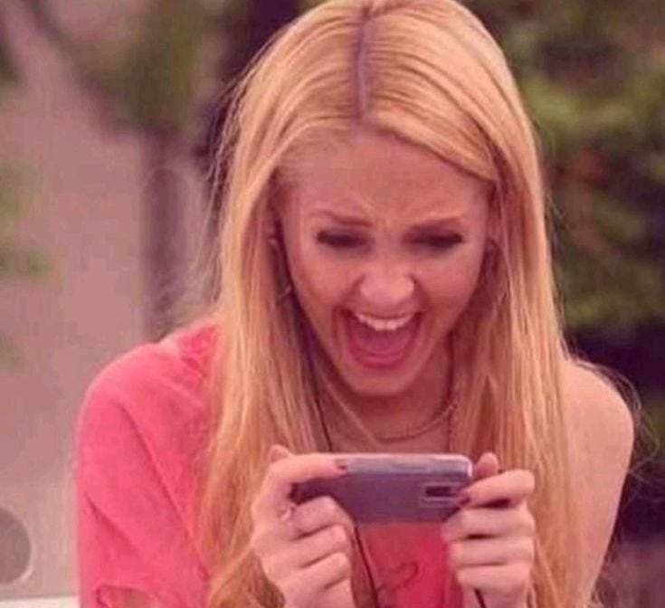 This may contain: a woman is laughing while looking at her cell phone and holding it in one hand