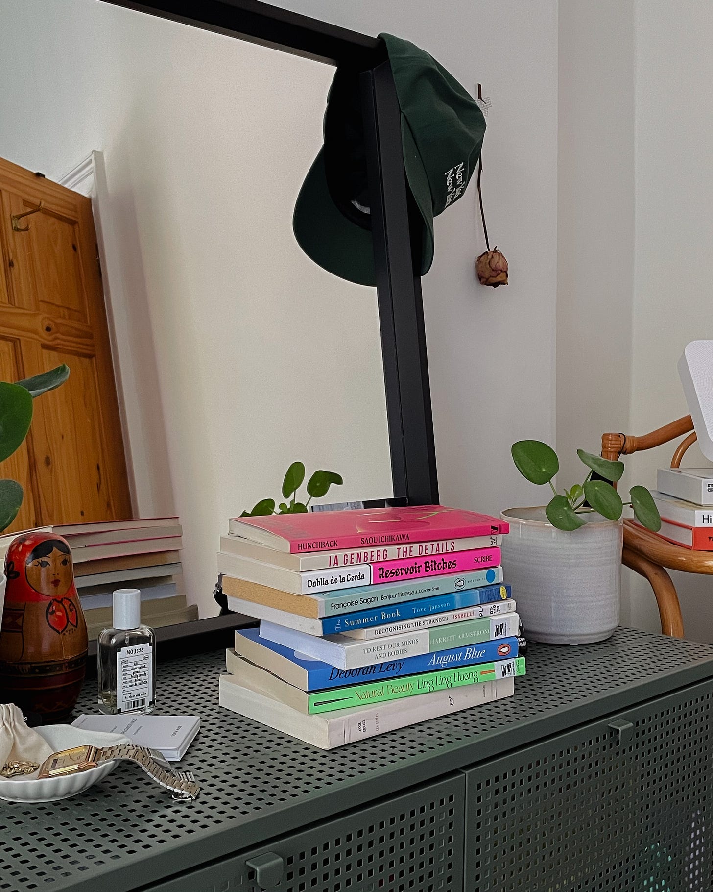stack of august reads on a green dresser, with plants, decor and a mirror in the background