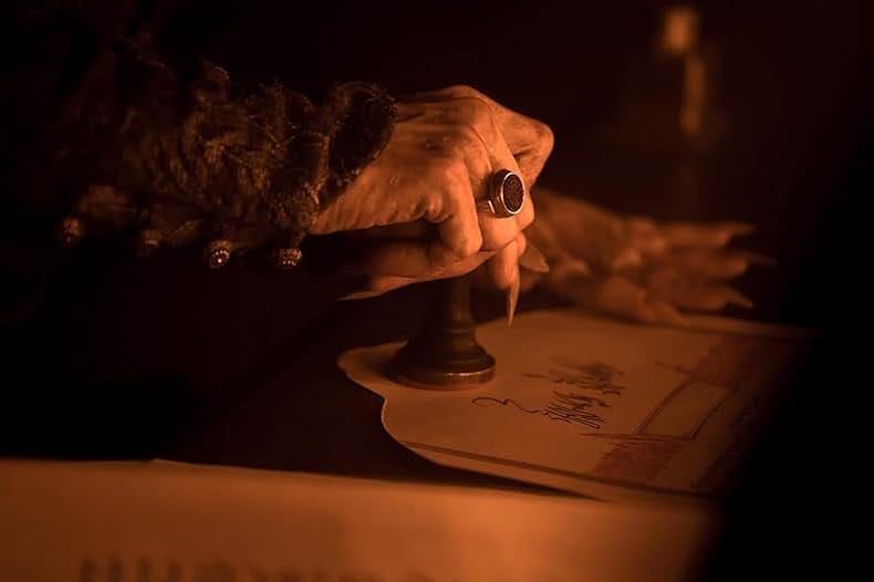 A still from the film. A monstrous hand with a large ring stamps an official document.