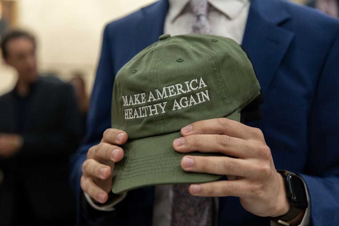A closeup of a pair of hands clutching a green baseball cap that says "Make America healthy again." 