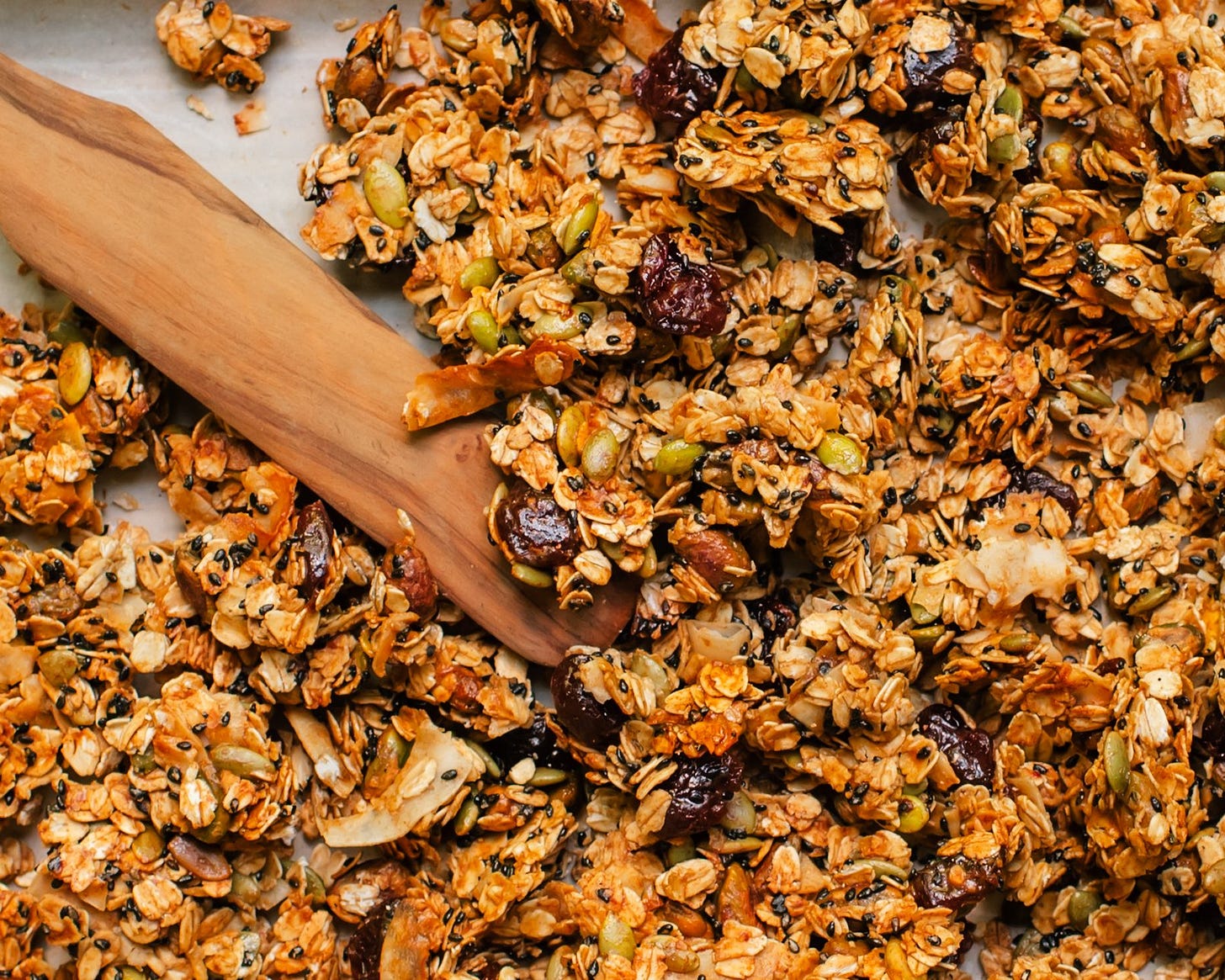 close up of granola with dried cherries, coconut chips, pistachios and pumpkin seeds on a sheet pan with a wooden spatula. close up of granola with dried cherries, coconut chips, pistachios and pumpkin seeds on a sheet pan with a wooden spatula.