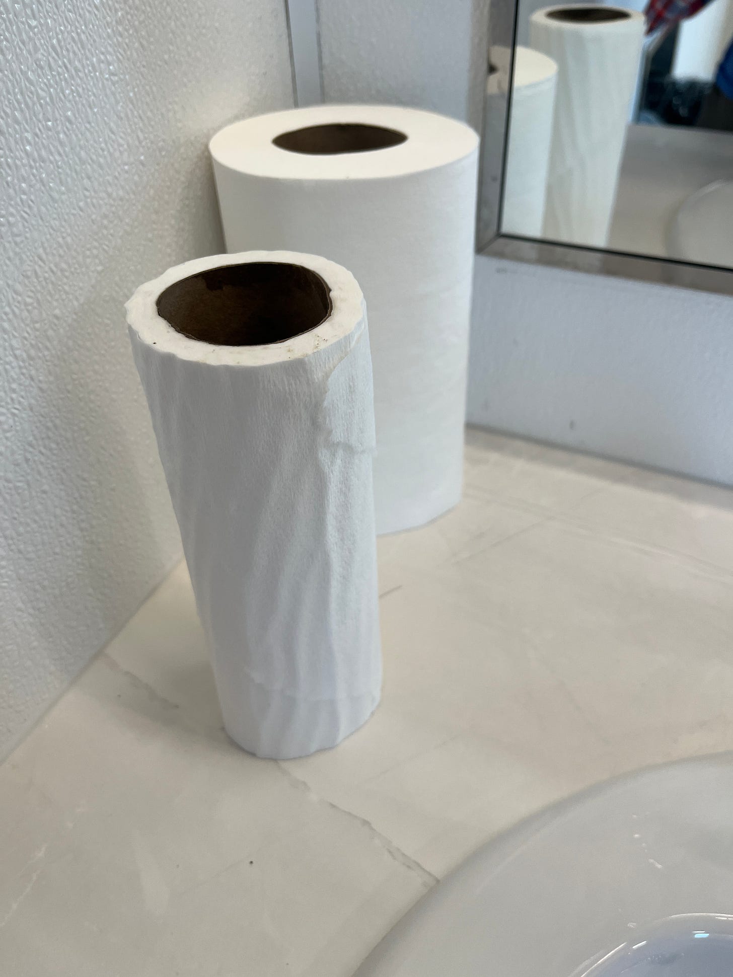Two rolls of paper towel, one full, one half-full, sitting on the counter of a public washroom