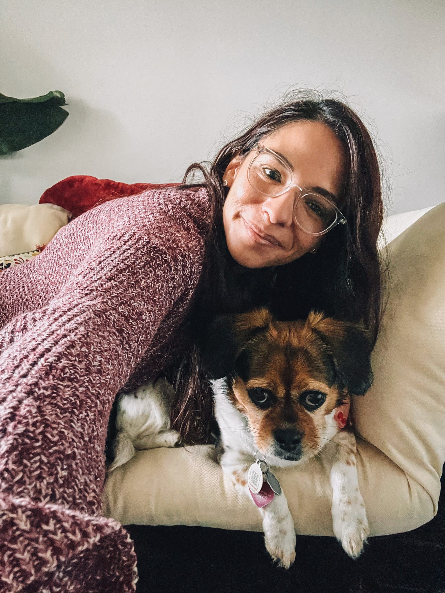 Selfie photo of woman sitting on couch with small dog next to her.