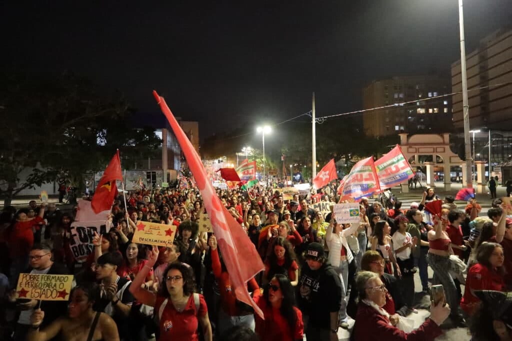 Crowd of demonstrators at night waving red flags and holding signs reading Diga Nao a Descriminacao and Pobre Formado e Perigo para o Estado Crowd of demonstrators at night waving red flags and holding signs reading Diga Nao a Descriminacao and Pobre Formado e Perigo para o Estado