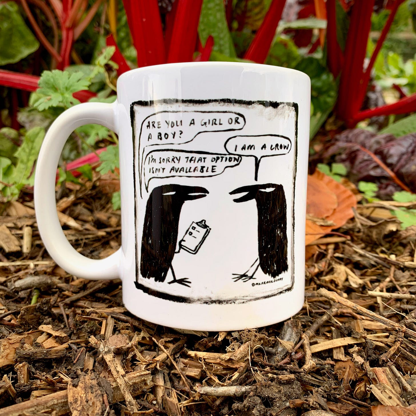 Photo of a mug featuring a comic of two crows, sitting on the ground, with what appears to be chard in the background Photo of a mug featuring a comic of two crows, sitting on the ground, with what appears to be chard in the background