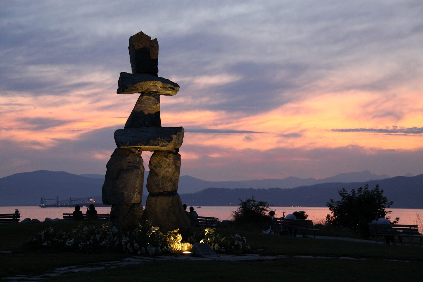 Photograph of large stone man-like structure, on a coast, against a dark and cloudy sky