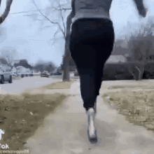 a woman is running down a sidewalk with a dog in her arms .