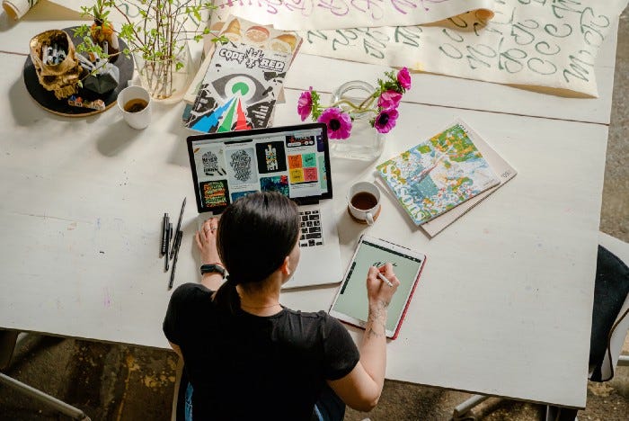 A woman with a tablet and laptop, looking at a number of design inspirations and drawing something at a table. A woman with a tablet and laptop, looking at a number of design inspirations and drawing something at a table.
