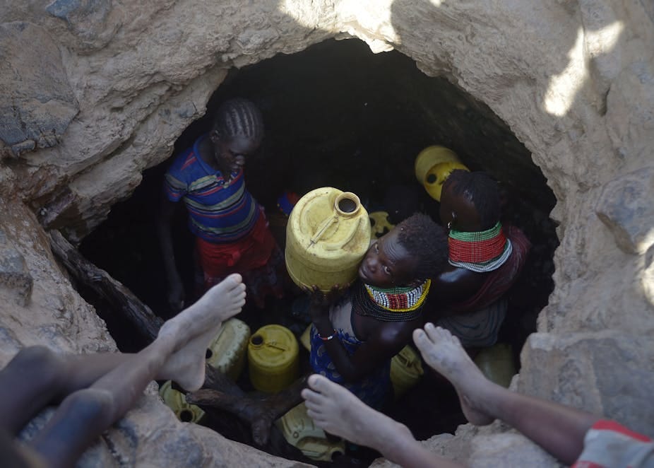 A young girl passes up a jerrycan filled with murky water trickling into a waterhole A young girl passes up a jerrycan filled with murky water trickling into a waterhole