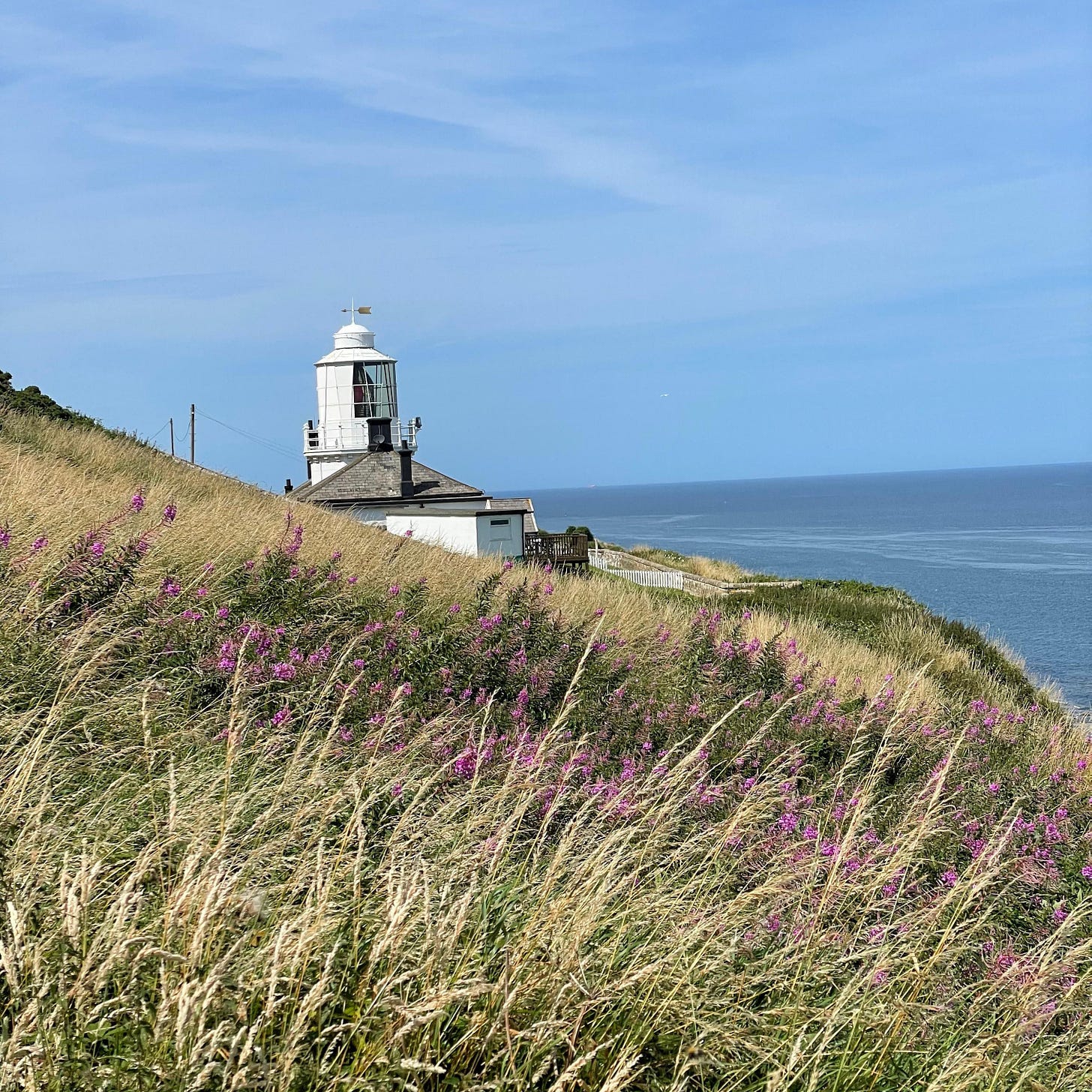 Whitby lighthouse, a tall white building, on the clifftops, the sea and blue sky in the background