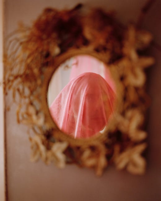 Une jeune femme, photographiée dans un miroir circulaire, le visage recouvert d'un voile rose brodé.