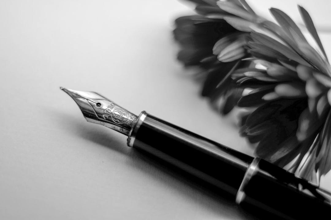 black and gold-colored fountain pen beside flower black and gold-colored fountain pen beside flower