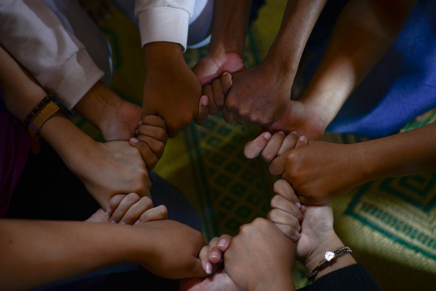 Hands linked in a circle, with different skin tones.