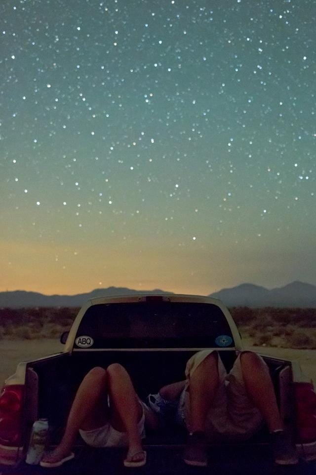 This may contain: two people sitting in the back of a pick up truck under a night sky with stars