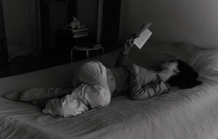 This may contain: a woman laying on top of a bed next to a child holding a book in her hand