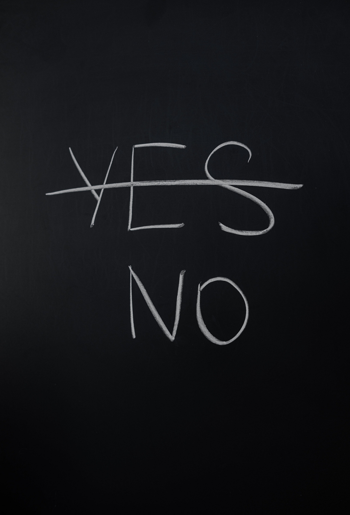 The word “yes” is crossed out on a chalk board in white chalk, leaving only the word “no” below it (also in white). The word “yes” is crossed out on a chalk board in white chalk, leaving only the word “no” below it (also in white).