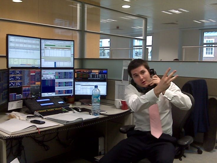This may contain: a man sitting at a desk in front of multiple computer monitors and talking on the phone