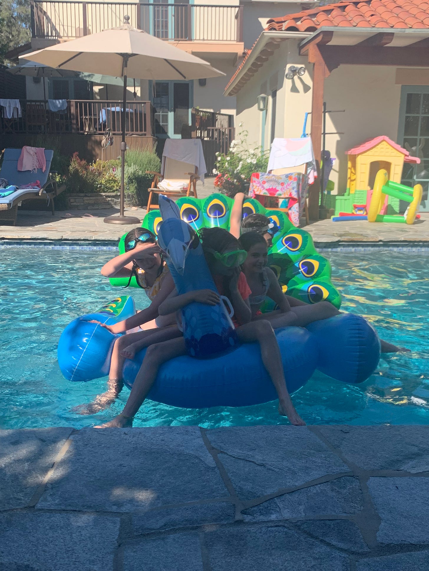 four kids barely hanging onto a peacock pool floatie