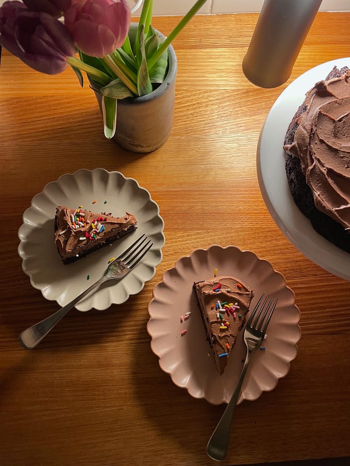 Saucepan full of beef and broccoli, garlic rice in a smaller pot alongside. A table lit with a lamp showing two slices of chocolate cake with salted chocolate icing.