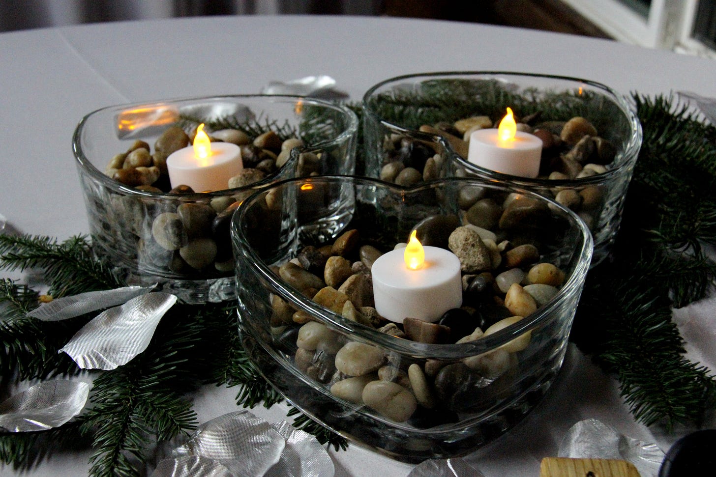 Heart shaped glass bowl containing rocks and a fake candle, surrounded by pine branches Heart shaped glass bowl containing rocks and a fake candle, surrounded by pine branches