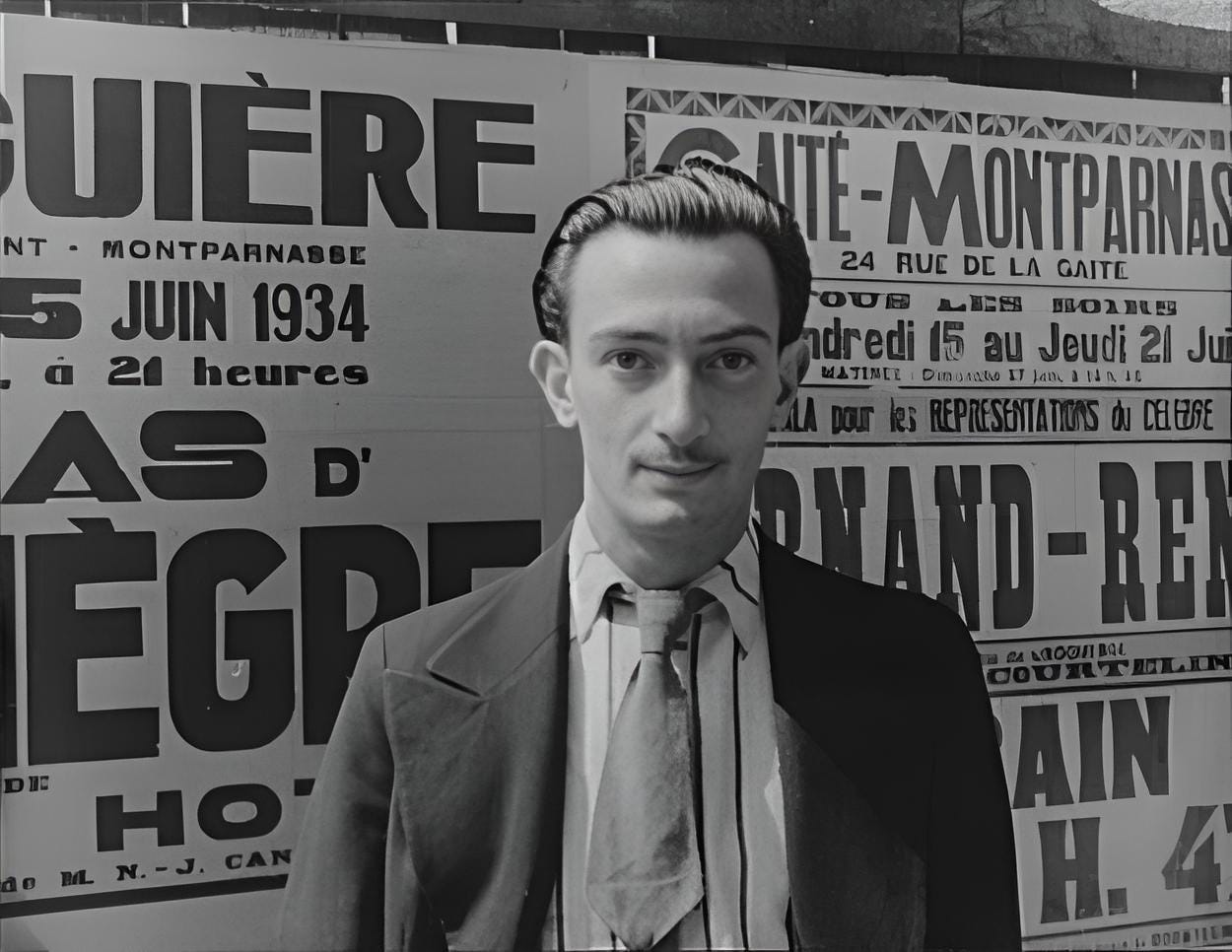 Salvador Dalí in a suit standing in front of a wall of Paris theatre posters. Salvador Dalí in a suit standing in front of a wall of Paris theatre posters.