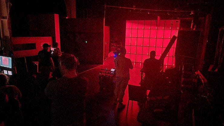 A film crew stands on set lit only by red light. A film crew stands on set lit only by red light.