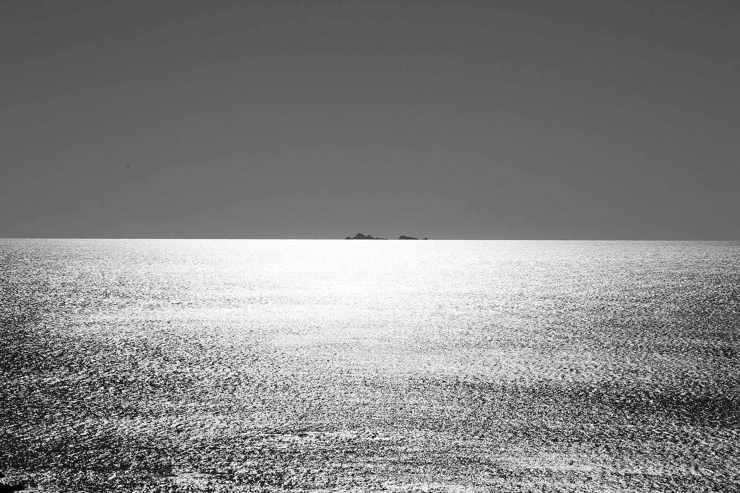 Photo of islands on a distant horizon seen across a sea reflecting the sun.