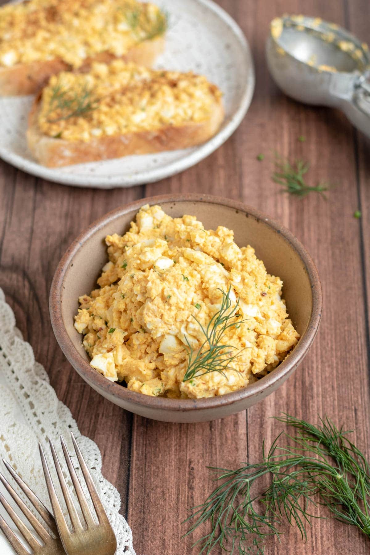egg salad in a small brown bowl garnished with dill. egg salad in a small brown bowl garnished with dill.