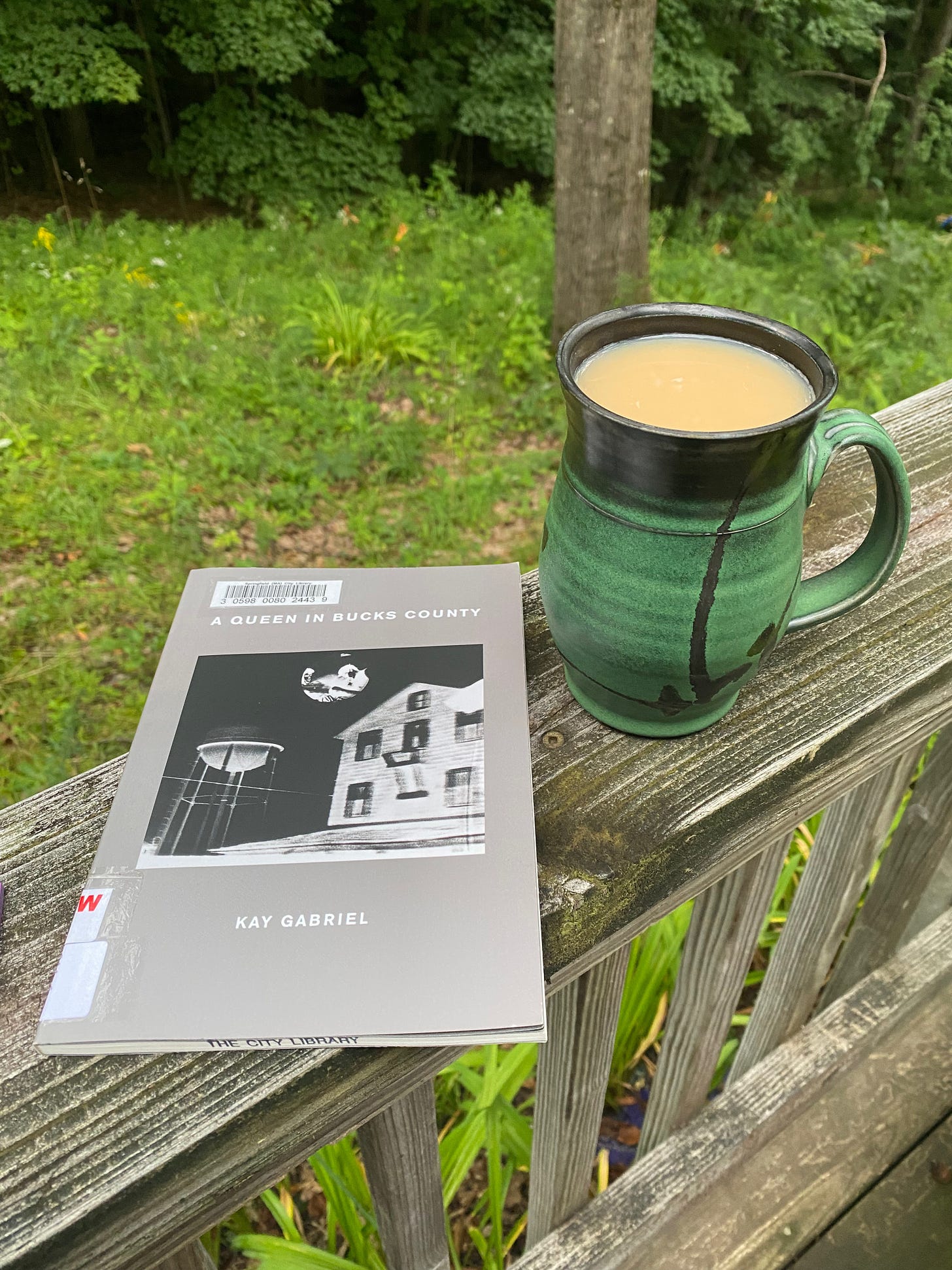 A green ceramic mug of tea and a book of poetry sitting on a porch railing.