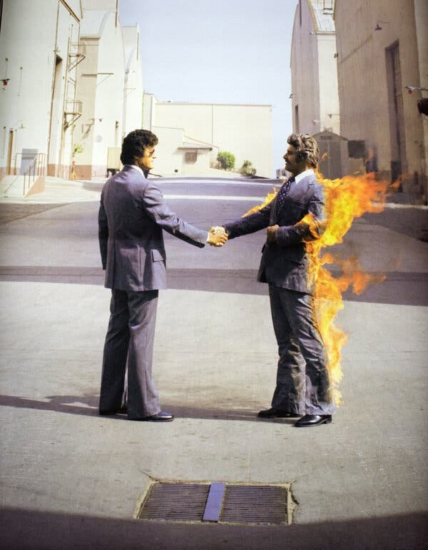 The front cover of the album “Wish You Were Here" features two men in suits. They are shaking hands, and one of the men is on fire. 
