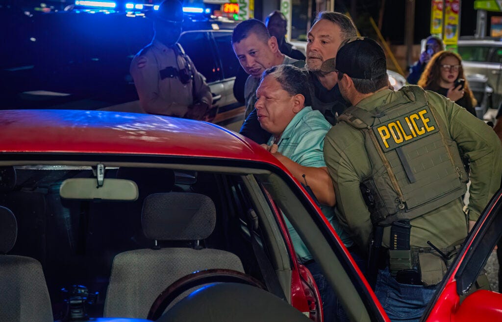 Three agents push the man against his car as a Tennessee Highway Patrol officer looks on. (John Partipilo/Tennessee Lookout)