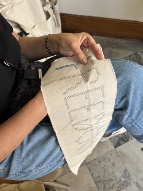 hands working with fiber and canvas spelling out words: Forgive, Freedom, Queer