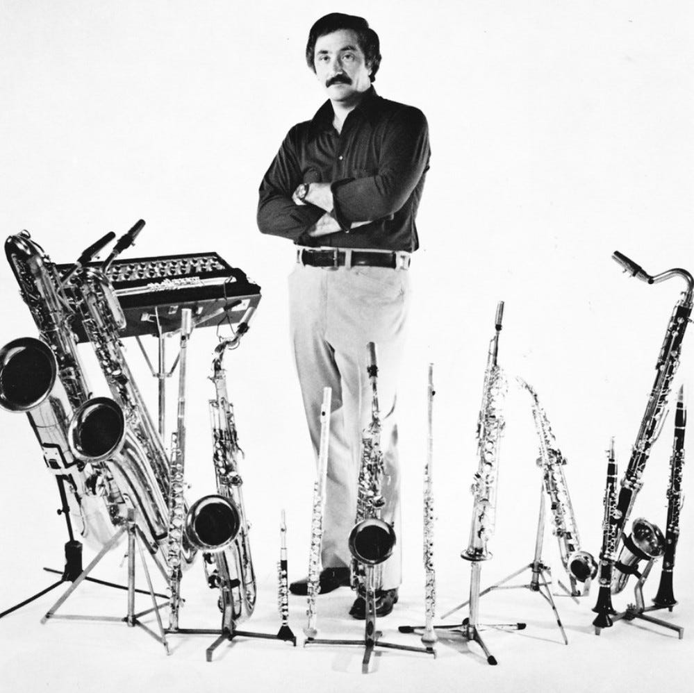 Musician Nick Brignola stands behind a row of 12 instruments -- saxophones, clarinets, and fluts in widely varying sizes.
