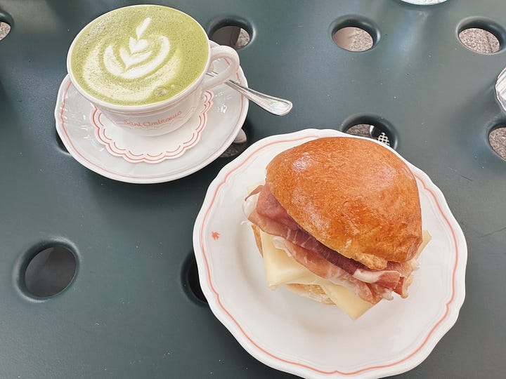 Slice of layered chocolate Gianduia cake and paninetti with prosciutto and cheese beside a matcha latte at Sant Ambroeus, Aspen.
