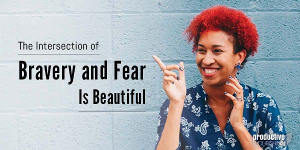 Woman behind a blue brick wall, pointing and smiling. Text overlay: The Intersection of Bravery and Fear is Beautiful Woman behind a blue brick wall, pointing and smiling. Text overlay: The Intersection of Bravery and Fear is Beautiful