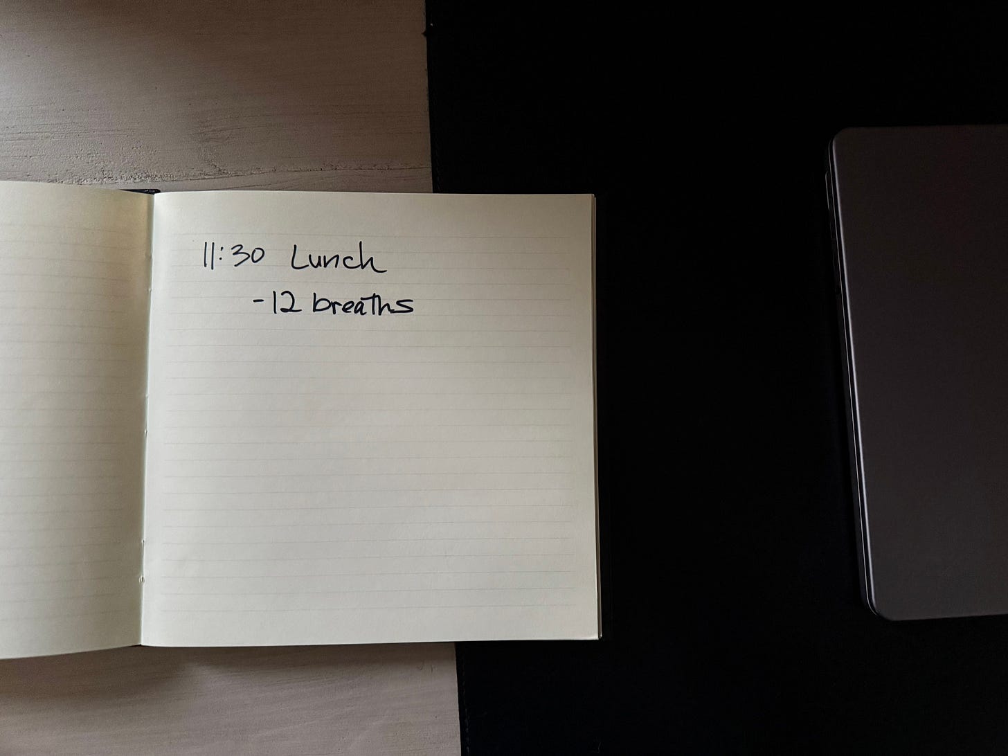 Closed laptop beside an open notebook on a desk; the notebook reads “11:30 Lunch” and “12 breaths.”