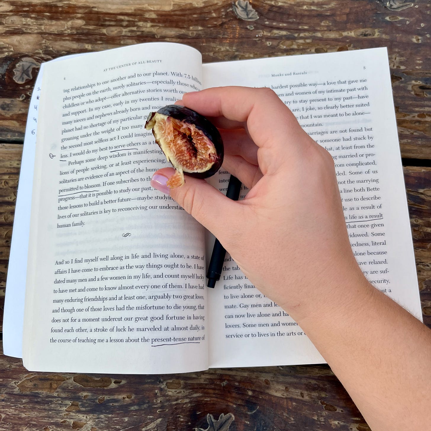 an open book with my hand resting on it holding a half eaten fig