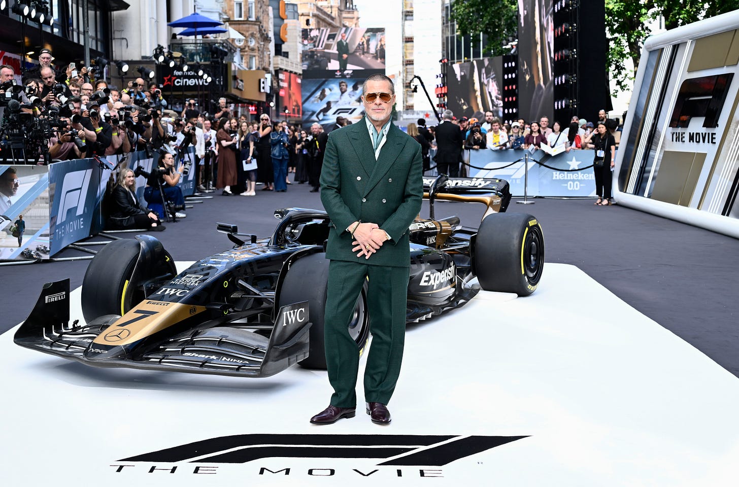 Brad Pitt wears a green suit and dark sunglasses, posing for photos in front of a replica F1 car outside Cineworld Leicester Square, during the European premiere of F1: The Movie